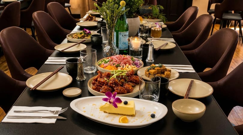 A long dining table set with multiple dishes, including dessert, and chairs in a restaurant.