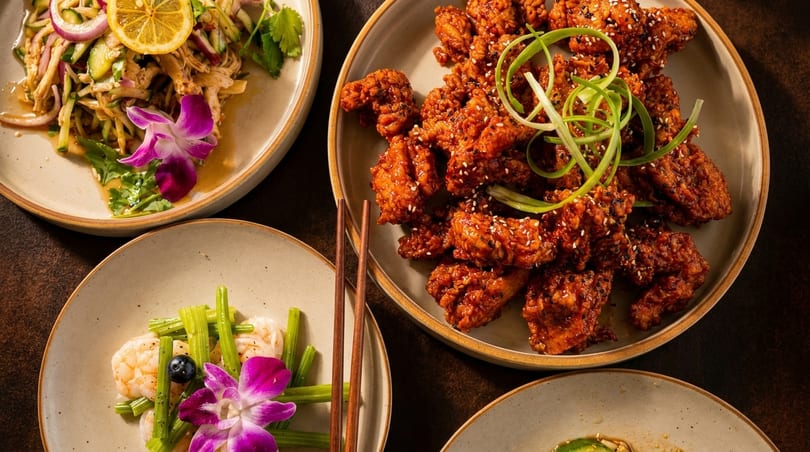An overhead view of three plates of Asian cuisine, including fried chicken, salad, and shrimp.