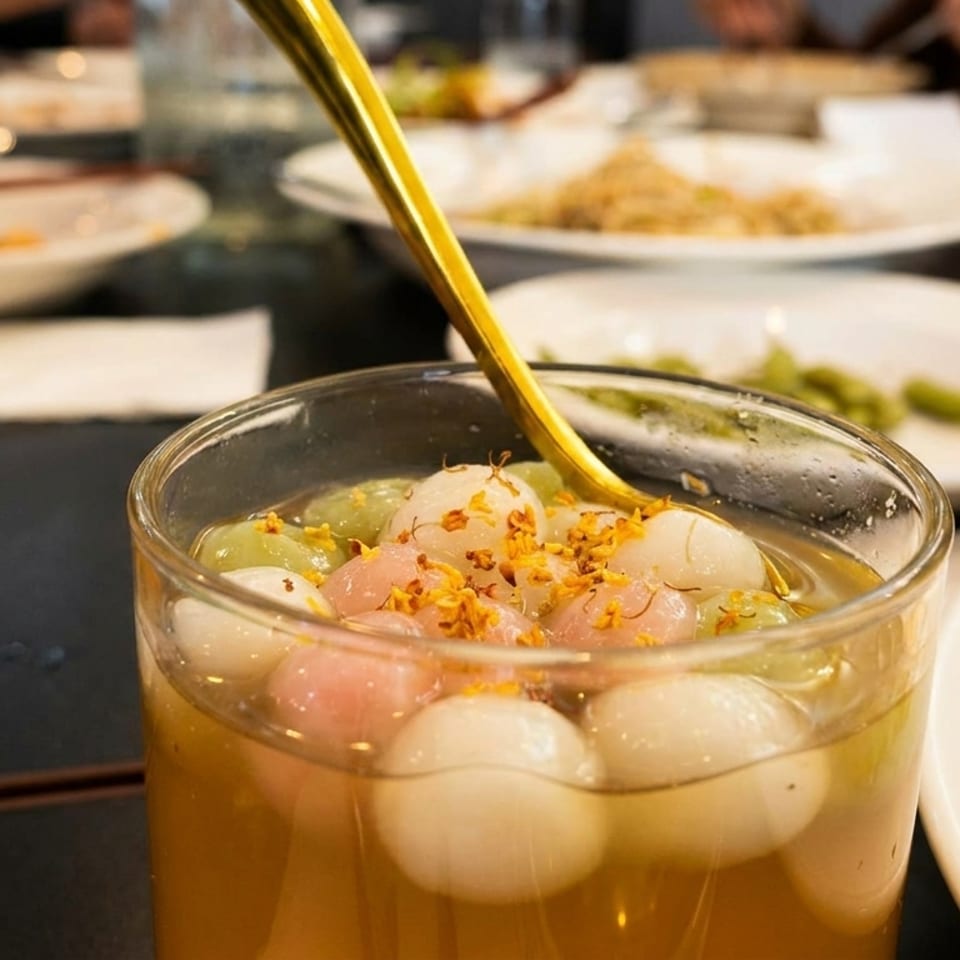 Close-up of a glass of tangyuan dessert with colorful rice balls and a golden spoon.